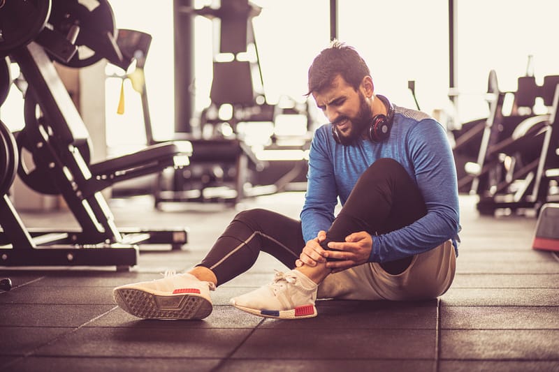 sports injuries, man holding ankle on floor of gym